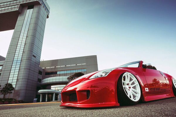 A red nissan near a gray building