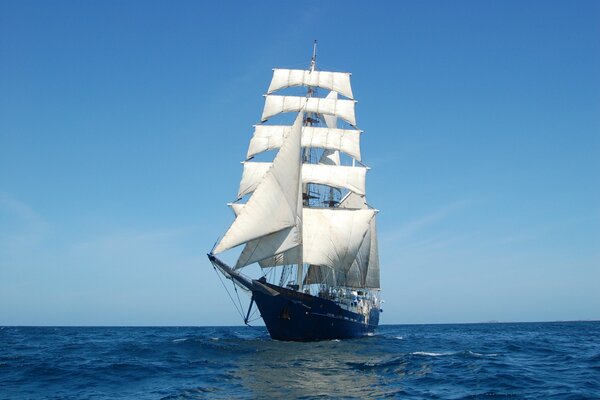 Barca a vela a due alberi con vele bianche contro il mare blu e il cielo blu chiaro