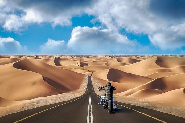 Motocyklista przecinający pustynie autostradą wśród wzgórz i barchanów