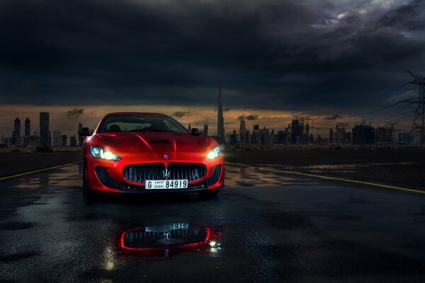 Un Maserati deportivo rojo con faros encendidos por la noche en el fondo de la ciudad