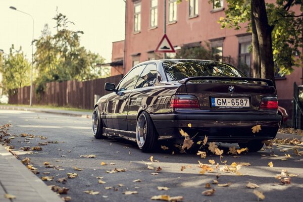 A black bmw car drives along the road with yellow leaves