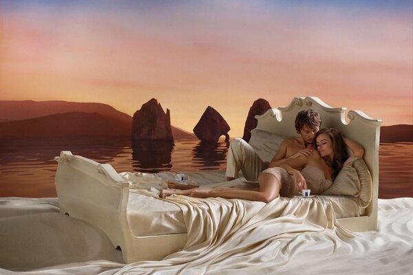 Łóżko na tle powierzchni morza. Zakochana para na białych prześcieradłach