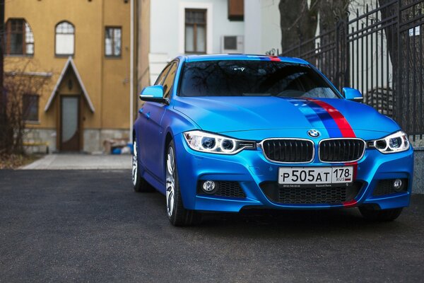 BMW azul con bandera en el fondo de las casas