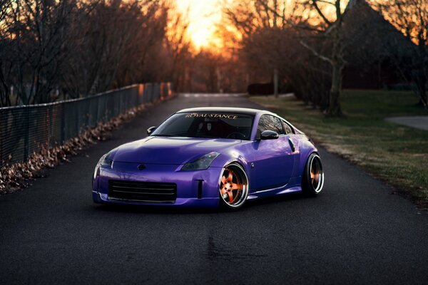 Nissan 350Z violet se trouve sur la route noyée dans le coucher du soleil