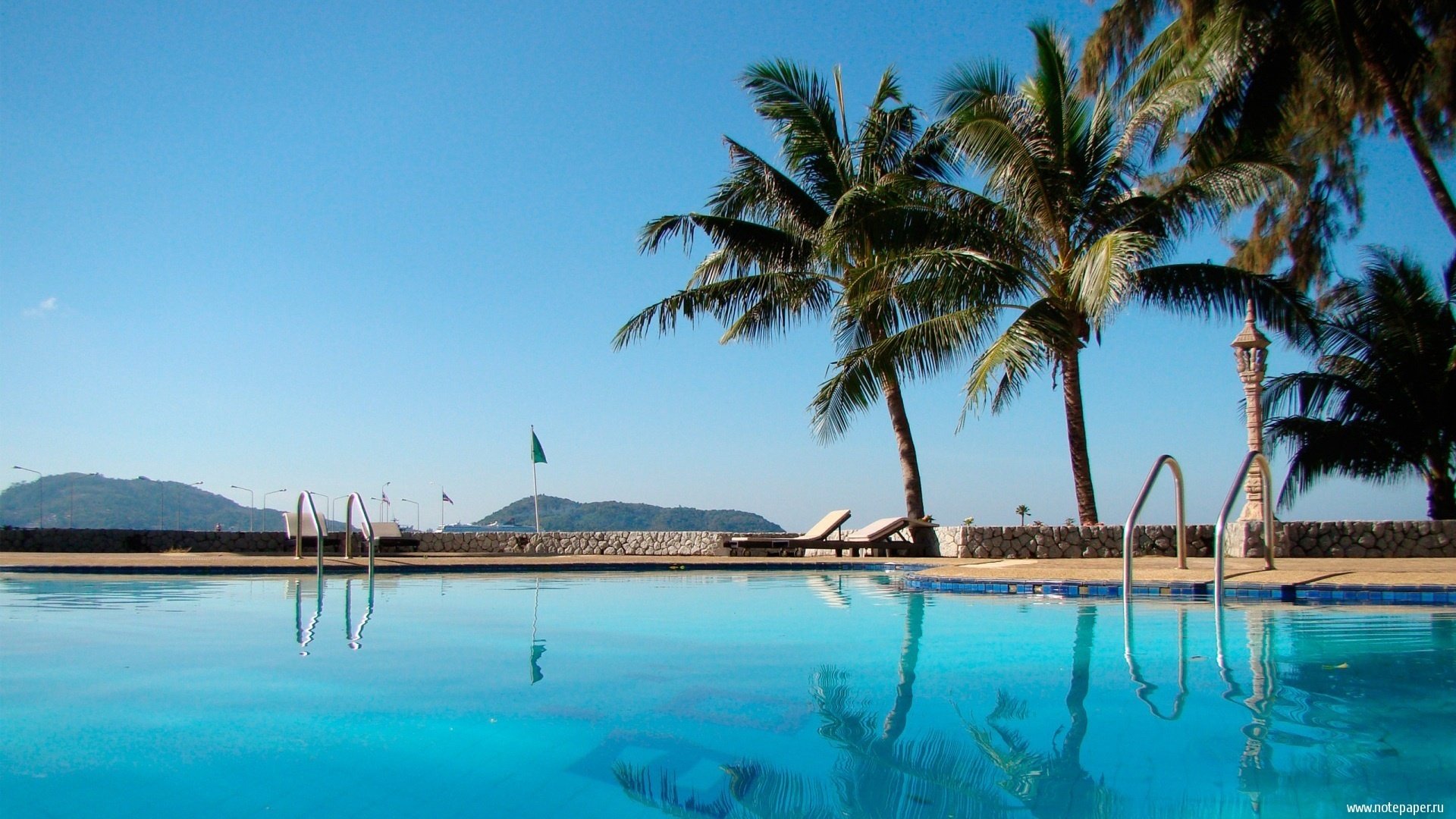 soleil piscine palmiers ciel chaises longues été chaleur eau claire pierres vue luxe montagnes arbres