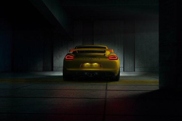 Porsche GT4 amarillo en una habitación oscura vista trasera