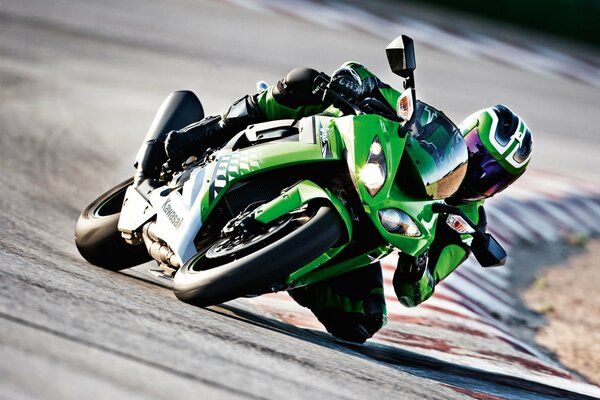 A green motorcycle enters a turn at speed