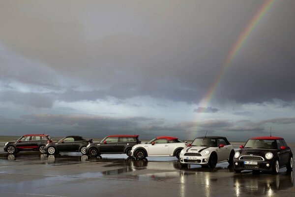 Varios autos mini cooper en medio de nubes y un arco iris después de la lluvia