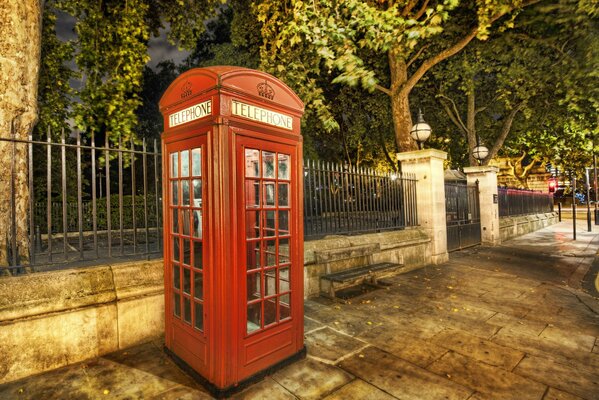 Cabina telefónica roja en la cerca del parque. Noche