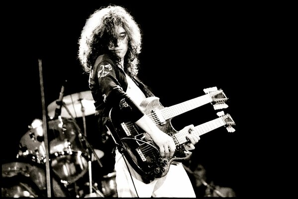 A long-haired musician with a guitar in white trousers