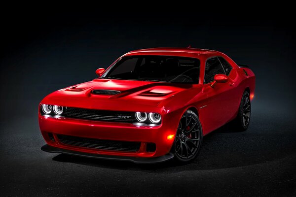 Red Dodge Challenger on a black background with headlights on