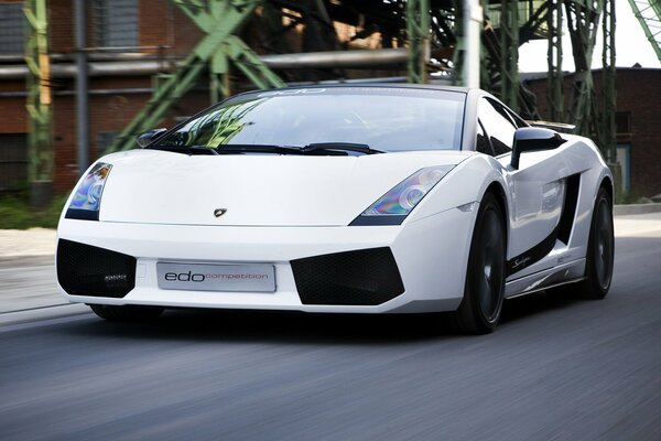 Superdeportivo Lamborghini en movimiento en una carretera asfaltada contra el fondo de un edificio de ladrillo