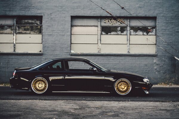 A black Nissan car is parked in front of a dilapidated building