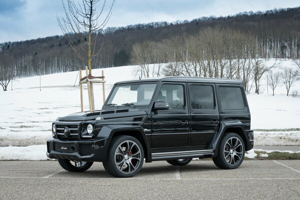 A black Mercedes on the street. There is snow and bare trees in the background. It looks like spring