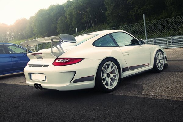 Foto eines weißen Porsche auf einem Parkplatz vor einem Hintergrund von grünen Bäumen