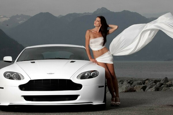 Coche blanco Aston Martin. La chica de blanco cerca del coche. Camino a las montañas