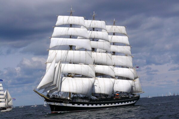 Le voilier Krusenstern navigue sur la surface de la mer sur fond de buissons épais qui poussent sur des nuages épais