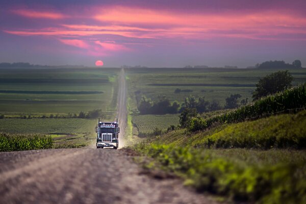 Auf dem Weg mit einem schönen Sonnenuntergang fährt ein Auto