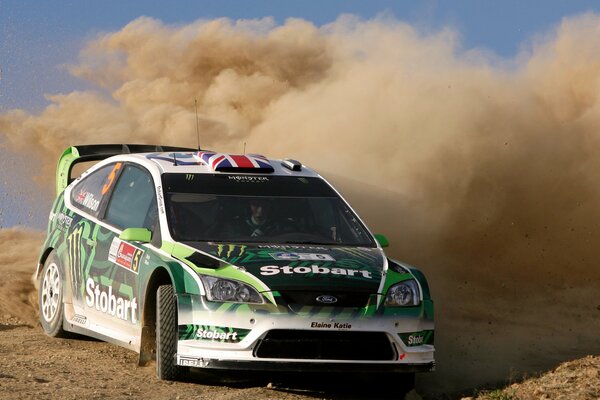 Photo of a Ford car skidding on a dirt road with a blue sky and a column of dust