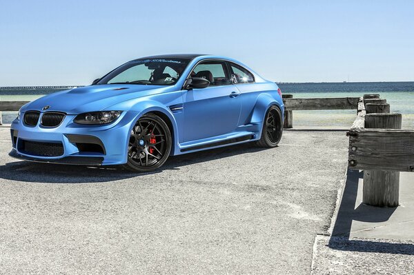 A blue car stands on the pier against the background of water