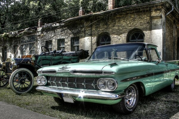 Vintage cars are parked on the grass outside the house