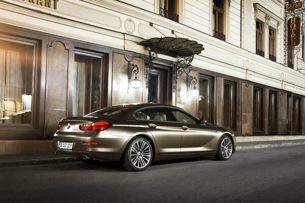 A BMW bronze-colored car is parked outside the building