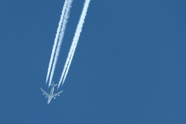 Samolot leci na błękitnym niebie pozostawiając biały ślad