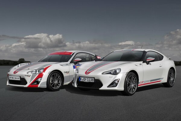 Two white sports cars on the road under a cloudy sky