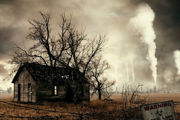 A house in a dangerous area with dried grass against a background of smoking pipes and greyness