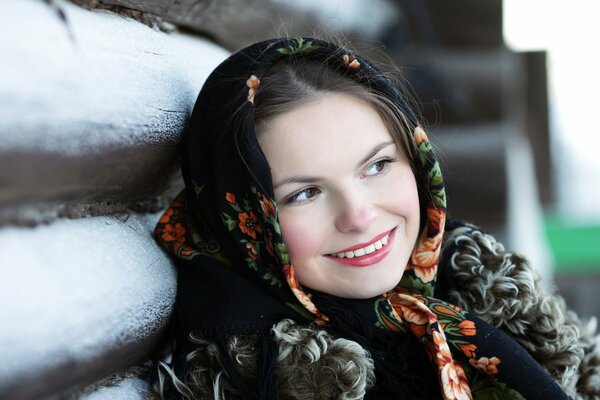 A Russian beauty in a headscarf smiles near the hut