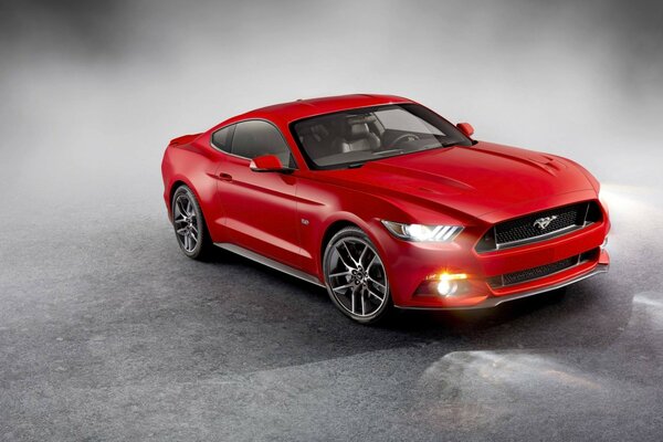 Un Ford Mustang rojo brillante con faros encendidos en el humo