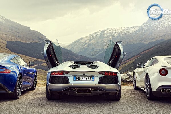 Three sports cars stand against the background of mountains. The second one has the doors open