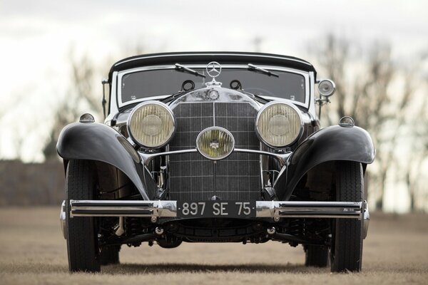 Un Mercedes-benz 540k negro se encuentra en la hierba seca en el espacio abierto