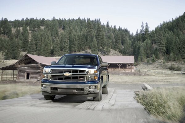 Blue Chevrolet in daylight on a village road surrounded by forest