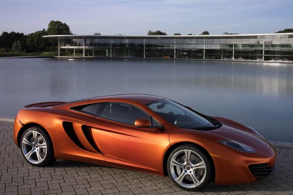 Оранжевый спорткар McLaren mp4-12cна фоне бассейна