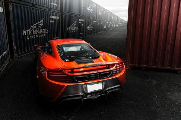 Une mclaren mp4-vx orange passe entre les conteneurs maritimes