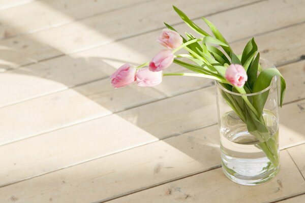 Tulpen in einem Glas Wasser auf einem Holzboden in der Frühlingssonne am Morgen