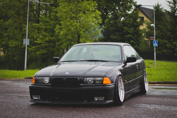 Tuned black BMW E 36 on a background of green trees