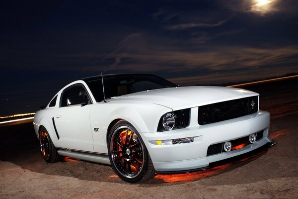 A white Ford Mustang is parked at night