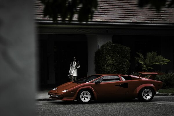 La chica sale de la casa y se acerca a un Lamborghini rojo