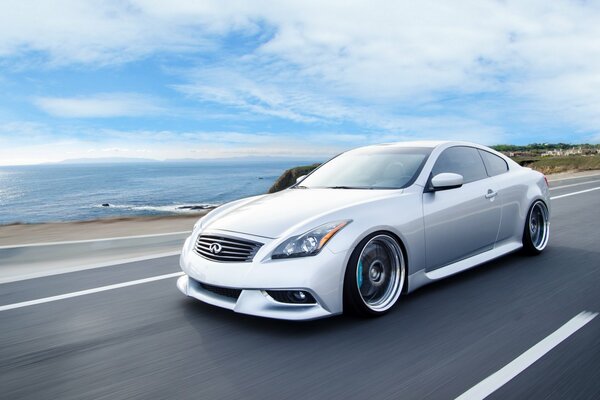 A white Infiniti coupe is moving along the road