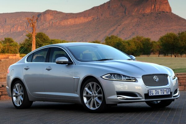 Silver Jaguar HF sedan on the background of mountains