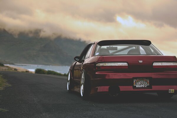 Red Nissan rear view driving along the road along the water