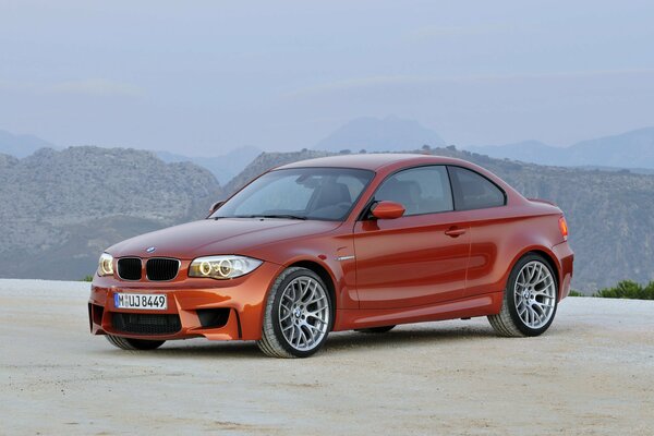 Orange bmw 1m passenger car on the background of mountains