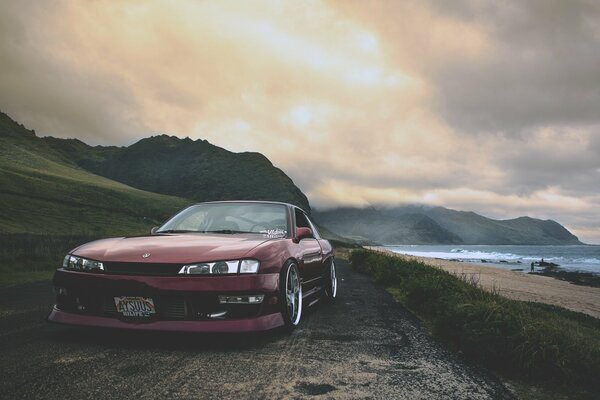 A burgundy Nissan car on the seashore