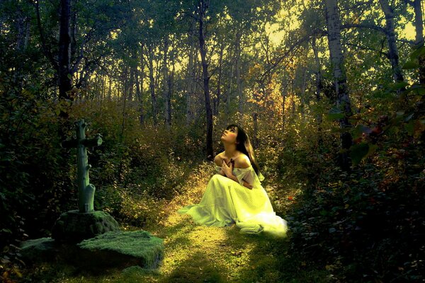 A girl in a white robe sits and prays in the forest