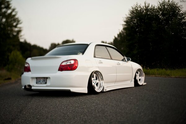 Tuned White Subaru impreza on the road against the background of trees