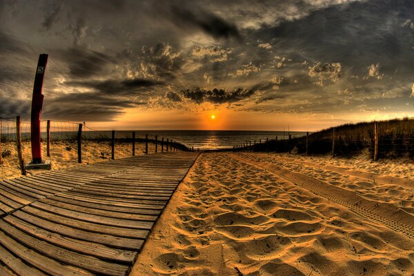 Une passerelle sur la plage mène au coucher du soleil sur la mer