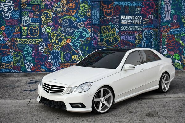 Biały Mercedes na tle ściany z graffiti