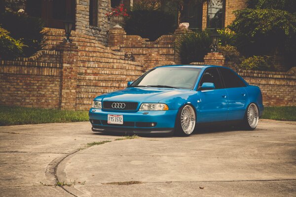 Une Audi A4 bleue devant une clôture en brique